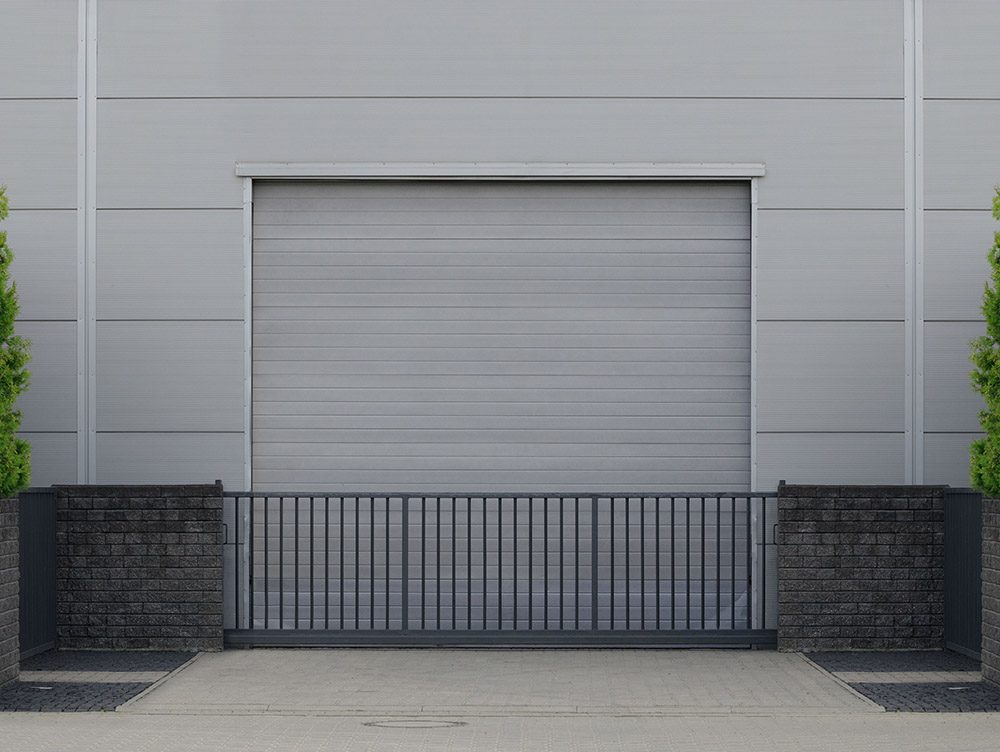 Roller door or roller shutter with application to factory, warehouse or hangar. Outside, trees on the sides